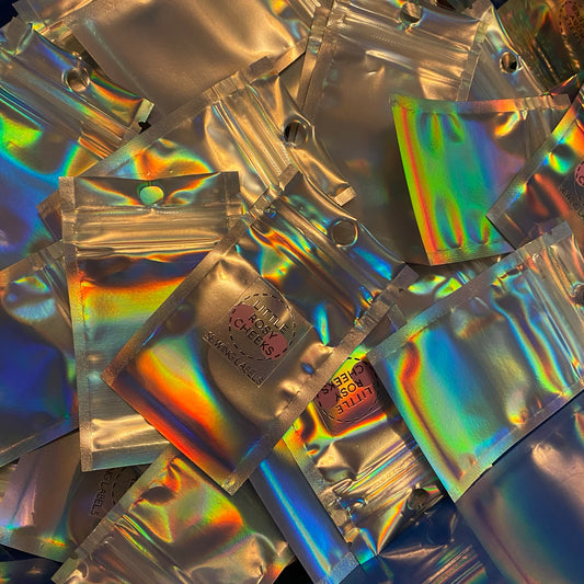 an empty pile of rainbow mylar plastic bags with a little rosy cheeks logo sticker central