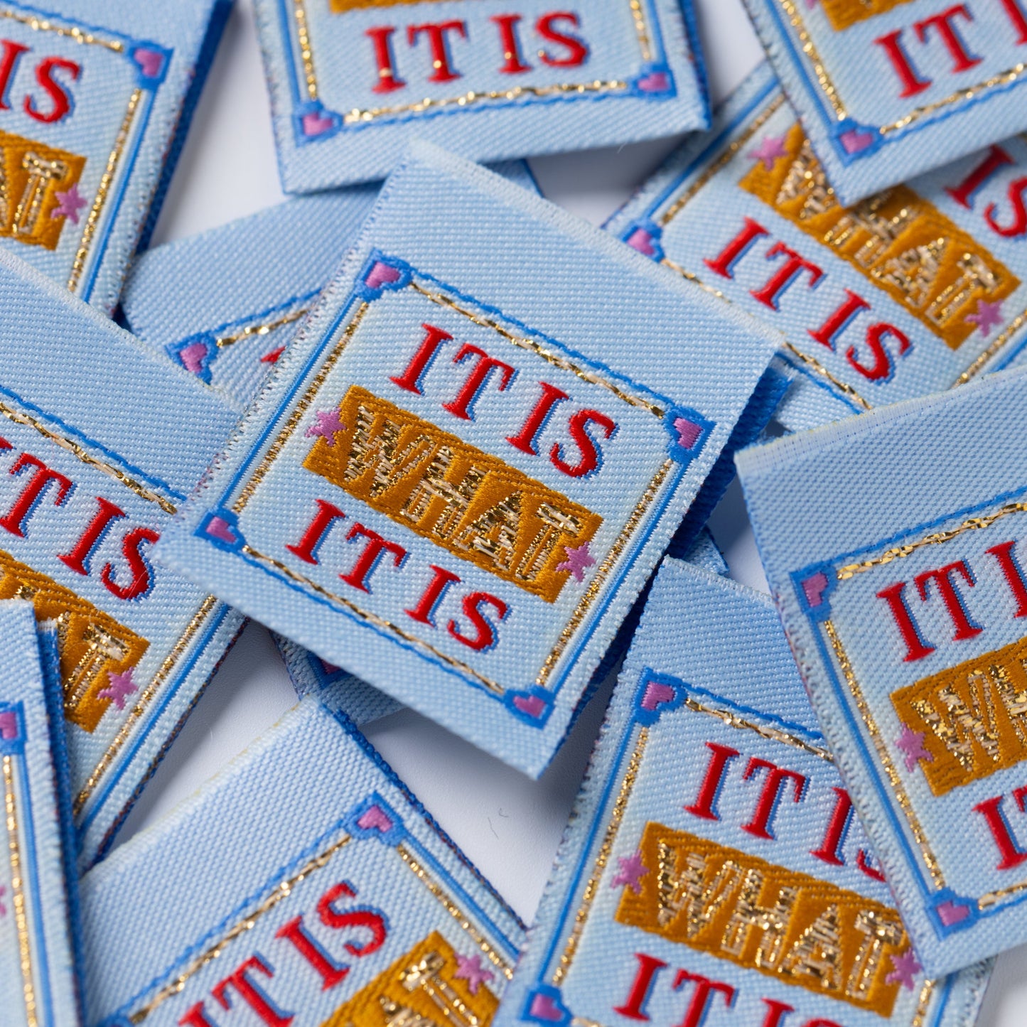 Multiple sewing labels with 'IT IS WHAT IT IS' text on a white background