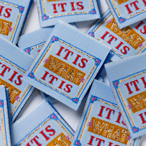 Multiple sewing labels with 'IT IS WHAT IT IS' text on a white background
