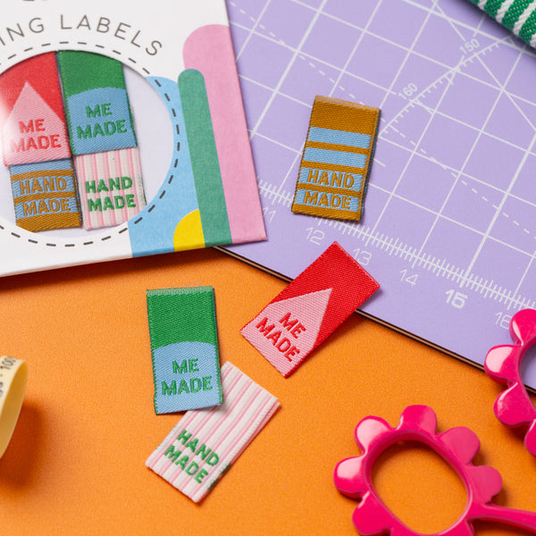 Colorful 'ME MADE' and 'HAND MADE' labels on a cutting mat with crafting tools.